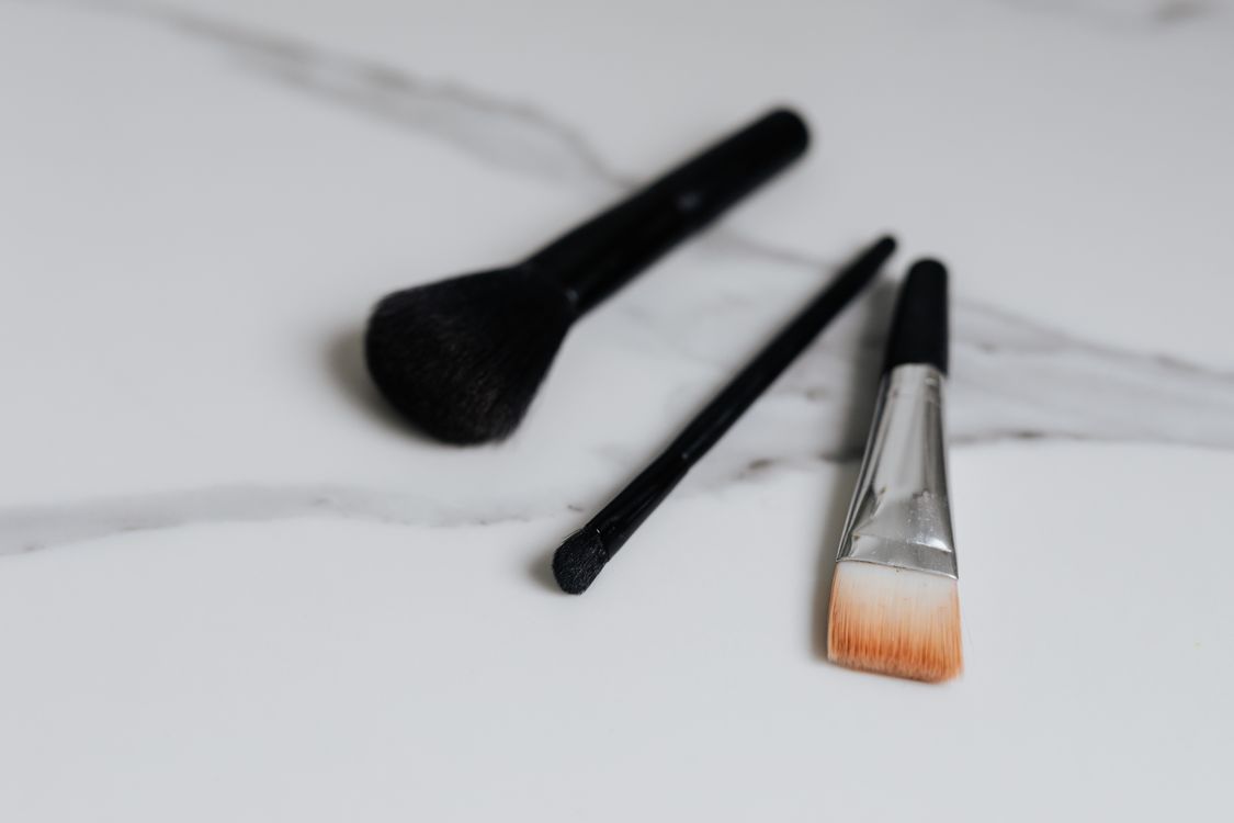 Tres brochas de maquillaje sobre una superficie blanca de mármol
