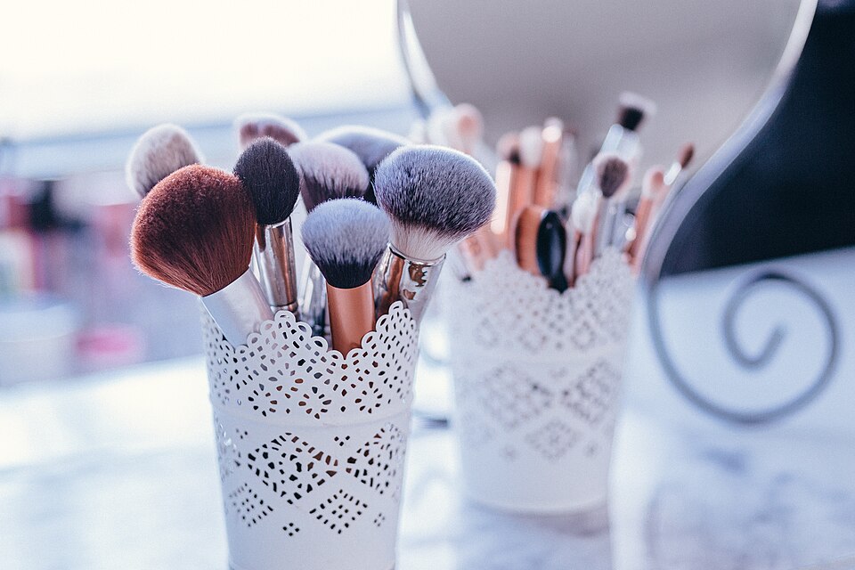 Brochas de maquillaje en recipientes blancos frente a un espejo