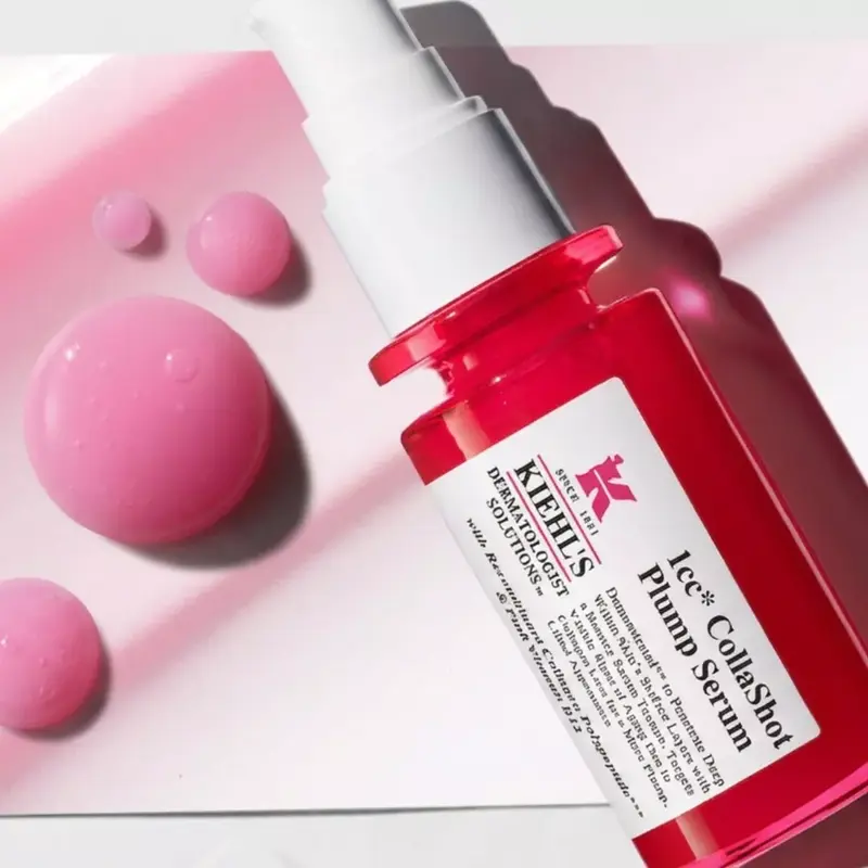 Sérum 1CC CollaShot Plump Serum de Kiehl's en frasco rojo junto a gotas de sérum rosado