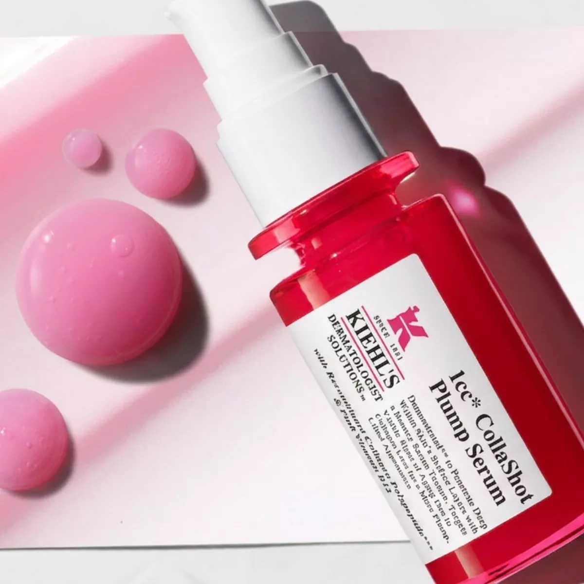 Sérum 1CC CollaShot Plump Serum de Kiehl's en frasco rojo junto a gotas de sérum rosado