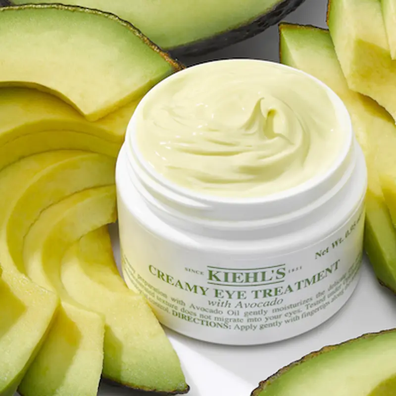 Crema de ojos con aguacate de Kiehl's en tarro abierto rodeado de rebanadas de aguacate fresco